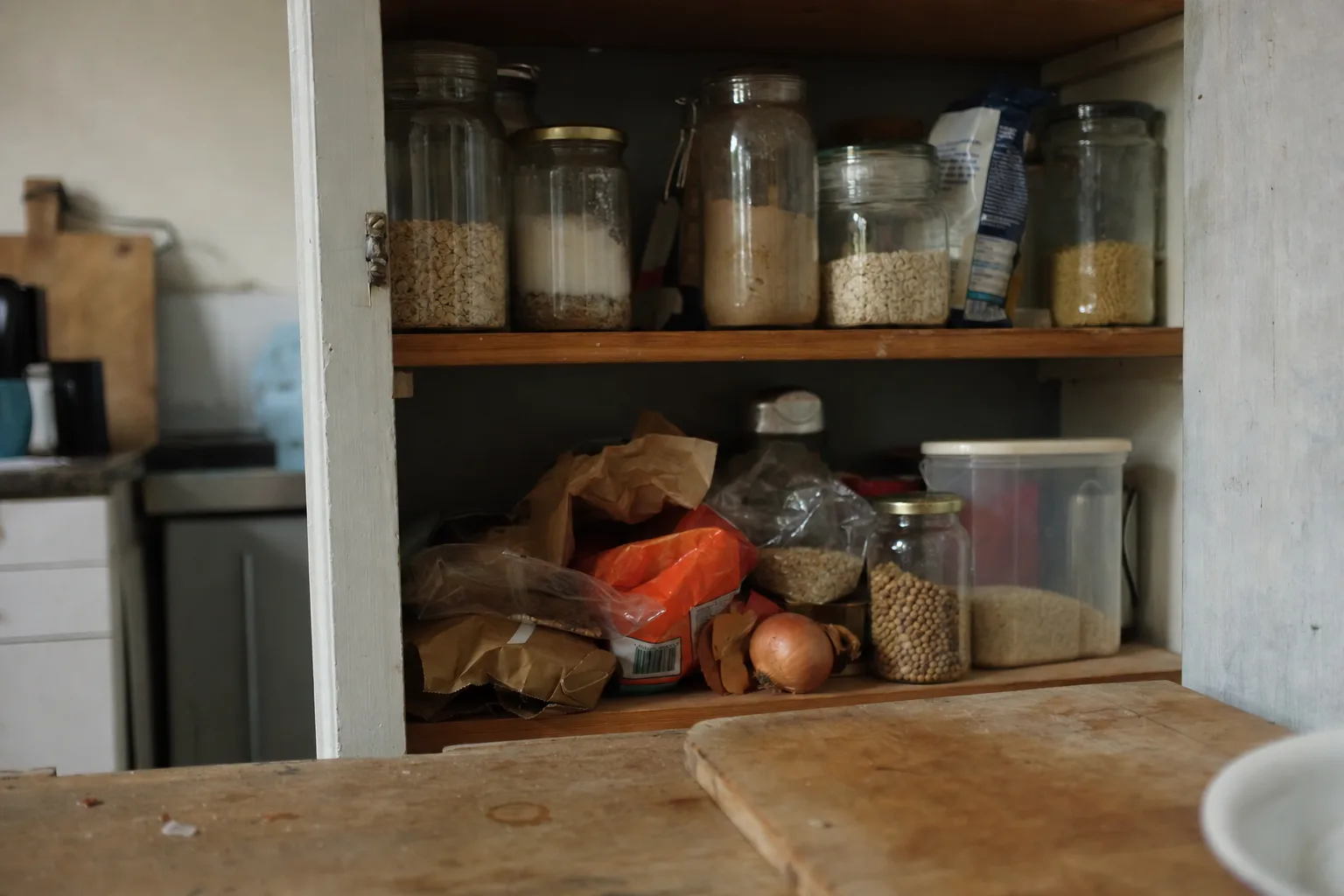 An open pantry shelf of mismatched jars and half-used bags with a couple of loose onions