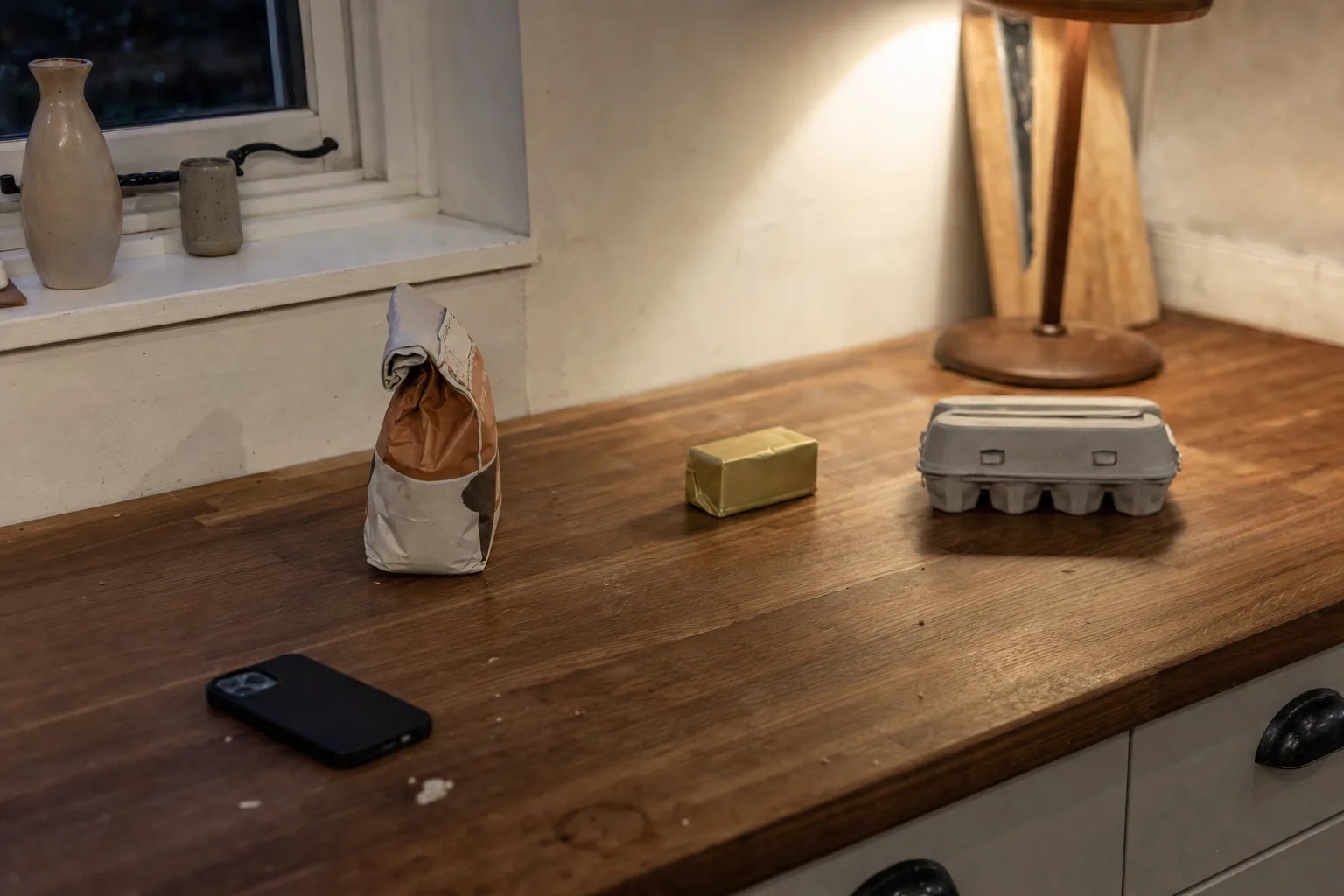 A few unopened ingredients spaced apart on an evening kitchen counter beside a phone lying face down