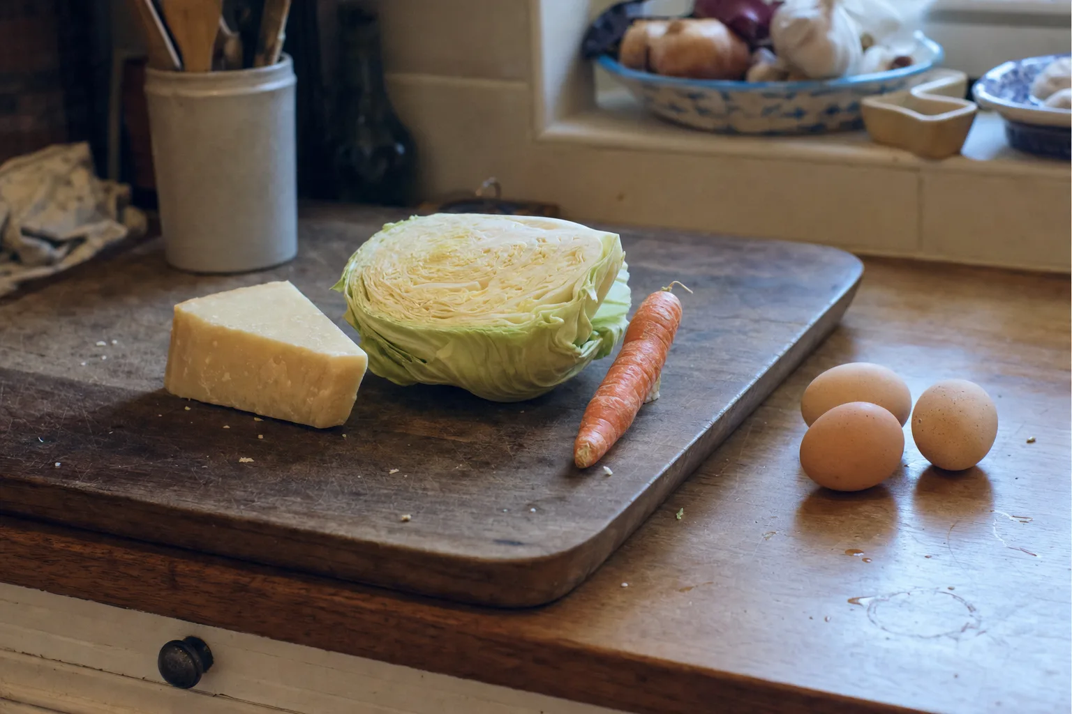 The odd leftovers of a real fridge on a counter: half a cabbage, three eggs, a heel of parmesan, one carrot